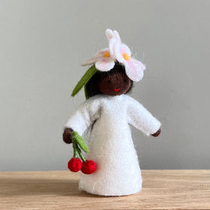 A felt Cherry Flower Fairy wearing a white dress and cherry flower on her head with dark skin tone holding a pair of cherries | © Conscious Craft