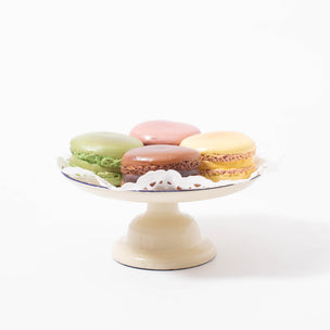 Four different coloured/flavoured resin macarons from Maileg on a hand painted cream metal cake stand with blue detailing and decorative paper napkin | © Conscious Craft