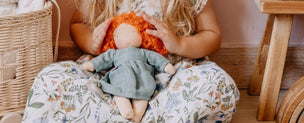Five handmade fabric dolls with soft cloth bodies and long hair in blonde, black, brown, red, and auburn, dressed in rust, dusty pink, blue-gray, and mustard yellow outfits, arranged side by side on a light gray background.