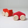 Grimm's Two red wooden toy cars with beige wheels on a light gray background