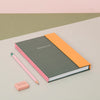 Notebook with orange and gray cover, pink pencil, and eraser on a multicolored background