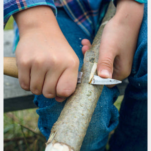 Person using a knife to cut a branch with a blurred background
