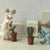 Two toy Maileg mice in a room with a washing machine and potted plants.