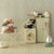 Miniature scene with a Maileg mouse on a washing machine, teapot, and ironing board against a patterned wall.