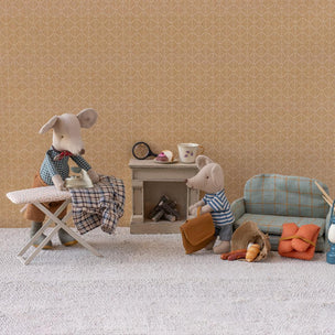 Two Maileg mice in a living room setting with furniture and accessories on a beige patterned wall background.