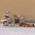 Two Maileg mice in a living room setting with furniture and accessories on a beige patterned wall background.