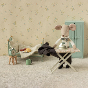 Miniature scene with a stuffed mouse character sitting at a table in a room with floral wallpaper.