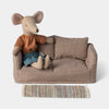 Maileg mouse sitting on a checkered sofa with a pillow and rug on a light gray background