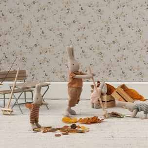 Maileg bunnies toys playing with autumn leaves and props on a light surface with floral wallpaper.
