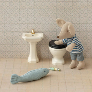 Miniature bathroom set with a toy mouse on a toilet, sink, and fish toy on a tiled floor.