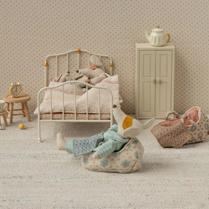 Maileg Miniature bedroom scene with a bed, toys, and furniture on a textured surface.