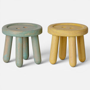 Two Maileg small round wooden stools with four legs, shown side by side on a light gray background. The stool on the left is painted in a distressed teal-green finish, and the stool on the right is painted in a distressed pale yellow finish.