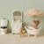 Miniature Maileg bathroom set with bathtub, toilet, and teddy bear under an umbrella against a patterned wall.