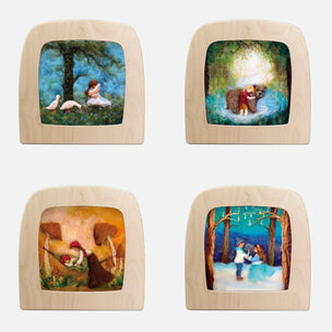 Four square wooden picture frames with rounded corners, arranged in a 2x2 grid on a light gray background. Each frame contains a different painted woodland scene: a girl sitting by ducks, a bear in a glowing forest, a figure among mushrooms, and a couple dancing in a snowy forest.