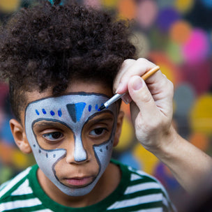 Child with face paint being applied against a colorful blurred background