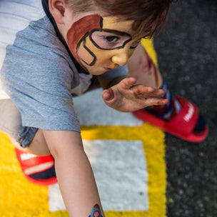 Child with superhero face paint and temporary tattoo on a yellow and white striped surface