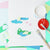 Colorful painting project with a frog design on paper, paintbrushes, and paint containers.