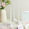 Decorative candles with floral patterns, a vase with flowers, and a birthday card on a light surface.