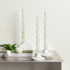 Three white candles with floral design on a metallic surface with a light background