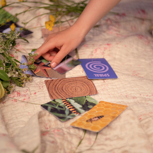 Hand interacting with tarot cards on a patterned surface with flowers.