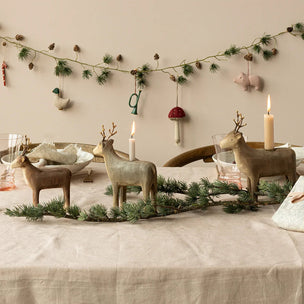 Decorative table setting with reindeer figurines, candles, and a garland on a neutral background.