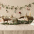 Decorative table setting with reindeer figurines, candles, and a garland on a neutral background.