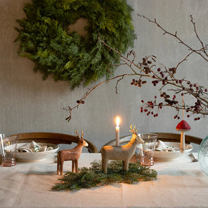 Decorative table setting with reindeer figurines, candles, and a wreath on a neutral background