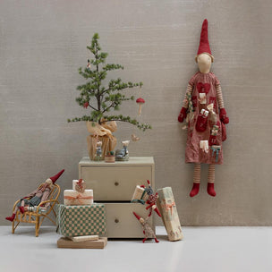 Decorative scene with small tree, gift boxes, and gnome figurines against a plain wall.