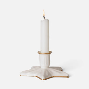 A white ceramic candle holder shaped like a five-pointed star, holding a lit white taper candle, set against a plain light gray background.