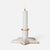 A white ceramic candle holder shaped like a five-pointed star, holding a lit white taper candle, set against a plain light gray background.