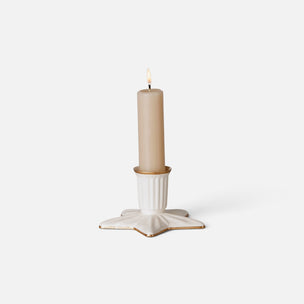 A single lit cream-colored candle in a white Maileg star-shaped holder with subtle gold-toned detailing, set against a clean white background.