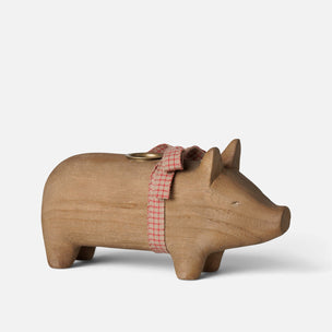 A small wooden Maileg pig figurine candle holder with a natural light brown finish, featuring a red and white gingham ribbon tied around its neck and a brass coin slot on its back, set against a plain light gray background.
