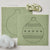 Felt Christmas ornament craft kit with two sage green felt sheets showing outline and embroidered pattern, a bundle of variegated thread, and white stuffing on a light beige background.