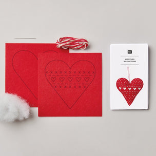 A heart-stitching kit laid out on a light gray background, including red felt sheets with heart embroidery guides, red-and-white twine, white cotton batting, and a white instruction booklet.