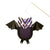 A bat-shaped hanging craft decoration made from black paper wings and body, with a patterned head in lavender, pink, and black, and white eyes, suspended from a wooden stick against a white background.