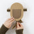 A person's hands holding a handmade cardboard robot toy against a clean white background. The toy is made from brown corrugated cardboard with accordion-style arms and legs, and a semi-circular cutout in the center.