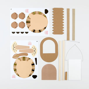 A children's craft activity kit featuring two printed sheets of animal face and body cutouts, along with several brown cardboard pieces, wooden sticks, and a white sign holder, arranged on a light gray background.