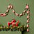 A red and white striped paper chain garland made of paper loops hangs against an olive green wall above a pine garland with warm lights and two red wooden horse figurines.