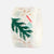 A roll of washi tape featuring a tropical green palm leaf pattern on a white base, with subtle pastel multicolor accents visible through the translucent tape.