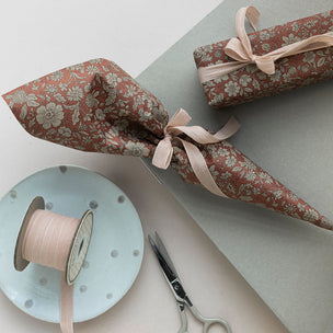 Two wrapped gifts with floral paper, a spool of ribbon, and scissors on a light surface.