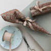 Two wrapped gifts with floral paper, a spool of ribbon, and scissors on a light surface.