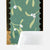 A close-up of a patterned card or notebook cover featuring a green background with mistletoe illustrations, scalloped black border details, and a peeled-back white backing layer.