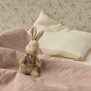 Toy rabbit on a bed with pink bedding and floral wallpaper