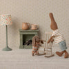 Two toy maileg rabbits in a room with a lamp, small table, and rocking chair.