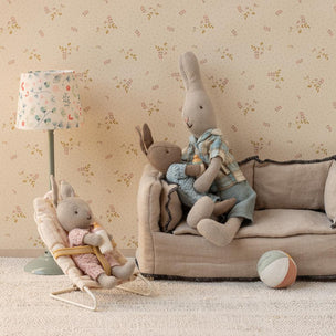 Maileg bunnies on a small couch with a lamp and ball in a room with floral wallpaper.