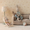 Maileg bunnies on a small couch with a lamp and ball in a room with floral wallpaper.