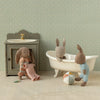 Three plush Maileg rabbit toys in a bathroom setting with a sink, bathtub, and towel.