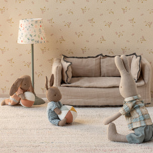 Three plush rabbit toys in a living room setting with a sofa and lamp.