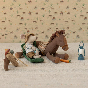 Maileg mouse in cowboy hat and boots sitting on a horse with a lantern and carrot on a patterned background