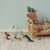 Children's room with a wooden crib, plush Maileg toys, and small figurines on a light green wall background.